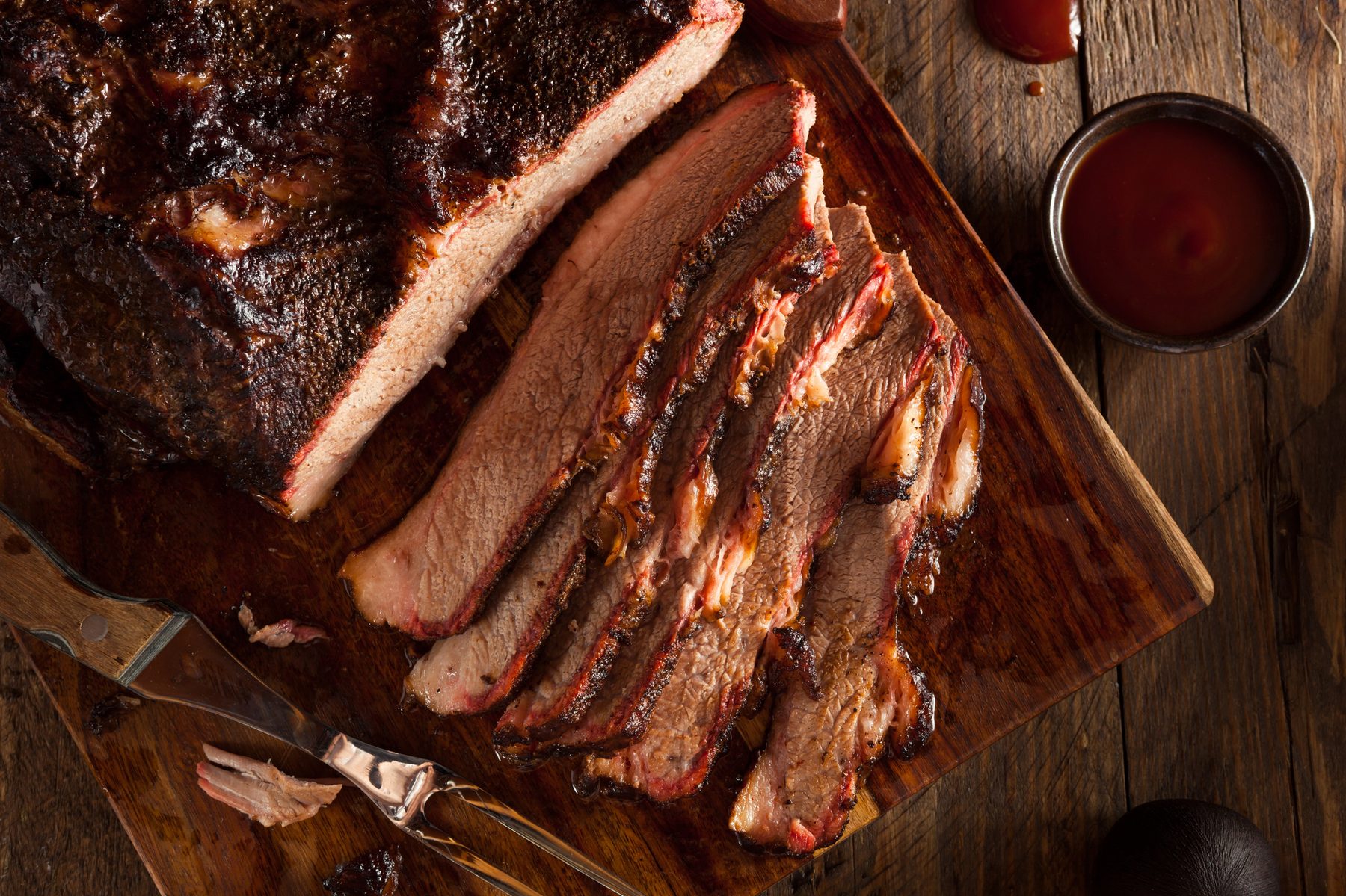 Sliced smoked brisket with charred bark on a wooden cutting board